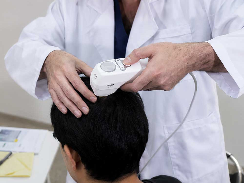 A photo of a doctor examining a patient's head with a hand-held medical tool. This image is being used to represent Patient Consultation.
